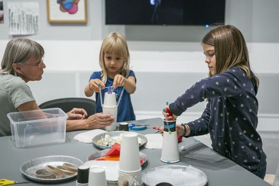 Berlinische-Galerie-Familien-Tag Foto: Zwei Kinder und eine Erwachsene sitzen um einen Tisch mit Bastelmaterialien. Die Kinder basteln Gebilde aus Pappbechern.